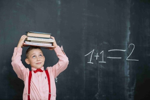 Chlapec s knižkami pri tabuli s matematickým príkladom
